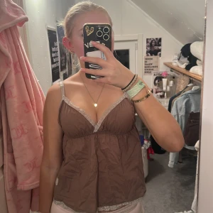 Brun Odd Molly linnetopp med spets - Supersöt brun linnetopp från Odd Molly med tunna axelband och v-ringning. Toppen har fina spetsdetaljer i ljusbeige längs urringning och nederkant samt broderad logga på sidan. Perfekt för en chill och trendig look.