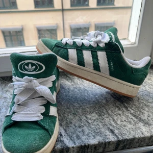 Adidas Campus 00s gröna sneakers stl 40 - Säljer mina gröna Adidas Campus 00s sneakers med klassiska vita ränder och breda vita skosnören. Ovandel i mocka och vit sula med gummidetaljer. Storleken är 40 (unisex). Skorna är i väldigt bra skick, bara använda fåtal gånger! Priset är 400kr, prutat och klart. Först till kvarn!🚀