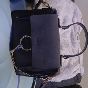 Svart Chloé handväska med guldkedja - Snygg svart handväska från Chloé i skinn med guldfärgade detaljer och kedja. Väskan har både handtag och axelrem, samt dragkedjor och magnetlås. Stilren design med rund guldring framtill och flera fack för smart förvaring.