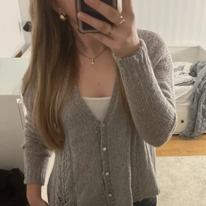 Grå stickad kofta med knappar - Mysig grå stickad kofta med v-ringning och pärlemorknappar framtill. 