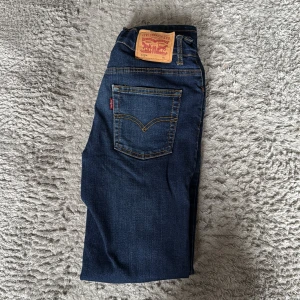 Levi's 512 Slim Taper jeans blå - Snygga Levi's 512 Slim Taper jeans i mörkblå denim med klassiska kontrastsömmar och femficksdesign. Märkespatch bak i midjan och röd Levi's-tagg på bakfickan. Perfekt smal passform med avsmalnande ben för en modern look.