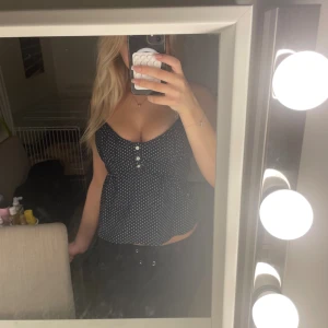 Brandy melville topp - Säljer en svart linnetopp med vita prickar och tre dekorativa knappar framtill. Toppen har v-ringad urringning. Den har one size men passar mig som har s 