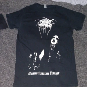 Darkthrone Transilvanian Hunger t-shirt - Svart t-shirt med vit tryck från Darkthrone, med ikoniskt Transilvanian Hunger-motiv på framsidan och stor grafisk print på baksidan. Klassisk passform och crewneck. Perfekt för dig som gillar black metal och vill sticka ut med en fet bandtröja.