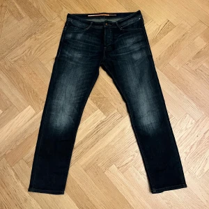 Mörkblå jeans från Jack & Jones - Snygga mörkblå jeans från Jack & Jones med klassisk femficksdesign och snygga urtvättningar  framtill. Jeansen har raka ben och slim passform, samt detaljerade bakfickor med broderad söm. Perfekta för en avslappnad stil. Hör av er vid frågor 