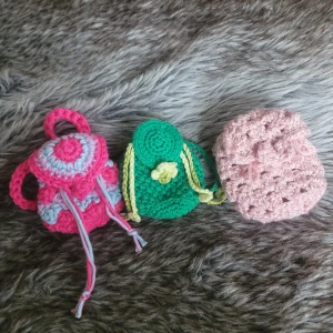 Handgjorda virkade miniryggsäckar - Tre söta miniryggsäckar i virkad bomull, perfekta som accessoar till gosedjur eller nyckelring. En är rosa och ljusblå med snörning, en grön med ljusgula detaljer och blomma, och en ljusrosa med bubblig struktur. Alla är små och färgglada, riktigt gulliga detaljer! 50 kr st