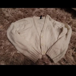 Vit kofta från H&M Divided XS - Mysig vit kofta från H&M Divided i storlek XS. Koftan är stickad med ribbade muddar och har tre knappar framtill. Perfekt för lager-på-lager och chill dagar. Enkel och stilren design som passar till det mesta.