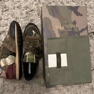 Valentino Rockrunner sneakers camouflage - Snygga Valentino Rockrunner sneakers med camouflagemönster i grönt, brunt, beige och svart. Skorna har detaljer i mocka och skinn, platt sula och rund tå. Endast skorna medföljer. Klassisk snörning och coola vinröda partier vid hälen. Perfekt för dig som gillar streetstyle och exklusiva märken.