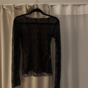 Svart långärmad spetsblus - Säljer en svart långärmad blus i transparent spets med blommigt mönster. Toppen har en smal passform och är perfekt för dig som gillar en stilren men ändå edgy look. Materialet är mjukt och följsamt, och den har en klassisk rund halsringning.