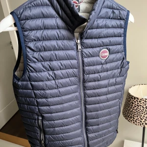 Blå dunväst från Colmar - Snygg blå dunväst från Colmar med quiltad design och dragkedja framtill. Västen har två praktiska fickor med dragkedja och ett rundat Colmar-märke på bröstet. Insidan är ljusgrå och materialet är lätt och smidigt, perfekt för lager-på-lager.