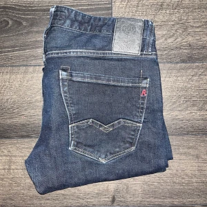 Replay Waitom jeans  - Snygga mörkblå Replay Waitom jeans med klassisk femficksdesign och kontrastsömmar. Raka ben och normal passform, tillverkade i slitstarkt bomullsjeansmaterial. Midja 42cm, längd 100cm. OBS jeansen är troligtvis uppsydda då jag anser att de sitter mer som L32 men utgå ifrån måtten. JAG SKICKAR EJ FLER BILDER NÄR JAG BÄR JEANSEN! för storleksguide hänvisar jag till måtten och för bättre inblick i passformen rekommenderar jag att googla på modellnamnet :) s3
