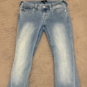 True Religion Joey Low Rise Flare Jeans - PRIS KAN DISKUTERAS - Snygga ljusblå jeans från True Religion, modell Joey Low Rise Flare. De har låg midja, bootcut-ben och klassiska fickor med lock och logoknappar bak. Jeansen är tillverkade i mjukt denim med coola slitningar framtill och detaljerad sömnad. Finns inga problem med dem helt nya, anledningen till att jag säljer de är pga längden. De är Storlek w26. 