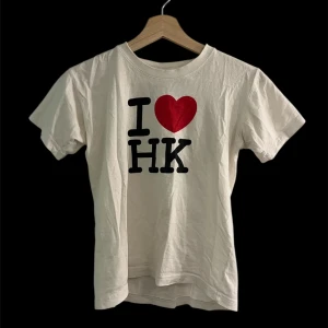 Vit I ❤️ Hong kong t-shirt - Vit t-shirt med trycket 'I ❤️ HK' på bröstet. T-shirten har rund hals och korta ärmar. Babytee med liten fläck framtill.