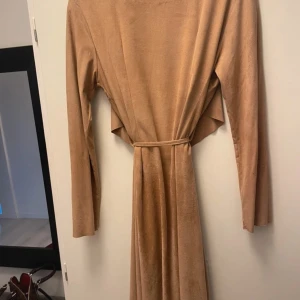 Beige långklänning från NLY Trend XS - Snygg beige långklänning från NLY Trend i mjukt material. Klänningen har långa ärmar, omlottmodell med knytband i midjan och en stilren look. Perfekt för dig som gillar minimalistisk och trendig stil.
