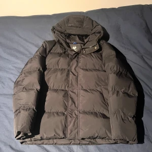 Svart pufferjacka från Ragwear, M - Svart pufferjacka från Ragwear i storlek M. Jackan har huva, dragkedja och tryckknappar framtill samt flera praktiska fickor. Tillverkad i syntetmaterial och designad för att hålla dig varm under kalla dagar. Perfekt för dig som gillar streetwear.