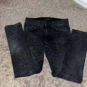Svarta skinny jeans från Nudie Jeans - Säljer ett par svarta skinny jeans från Nudie Jeans i storlek 28/28. Jeansen har klassisk femficksdesign, svarta sömmar och Nudie-loggan på bakfickorna.