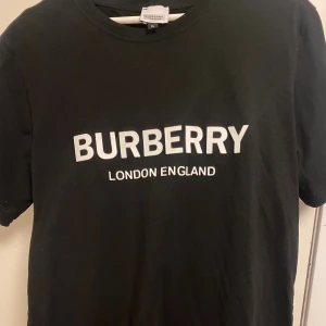 Burberry T-shirt logo  - Burberry T-shirt svart med vit logo typ, använd några gånger men i mycket bra skick. Gått ner i vikt så säljer av massa kläder storlek XL men är lite slim i storlek så sitter som L 