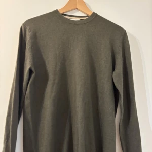 Mörkgrön stickad tröja Bruun & Stengade - En stilren mörkgrön stickad tröja från Bruun & Stengade i storlek S. Tröjan har rund halsringning och långa ärmar, perfekt för dig som gillar enkel och clean look. Materialet är en kashmir blanding