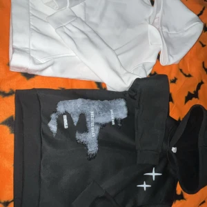 Svart och vit hoodie med tryck - Två hoodies säljes, en svart med coolt vitt tryck och textdetaljer på bröstet, samt en vit hoodie med tryck på ryggen. Båda har huva och långa ärmar, tillverkade i mjukt bomullsmaterial. Perfekt för dig som gillar streetwear och grafiska detaljer.
