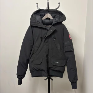 Canada Goose - Canada Goose Chilli Wack Bomber, storlek L Perfekt för kallt väder ner till -20°C.  •  Värmande anduckfyllning. •  Vattentåligt och vindresistent yttertyg i Arctic-Tech. •  Flera fickor: bröstfickor, ärmficka och inre fickor. •  Justerbar midja och manschetter för bättre passform. 
