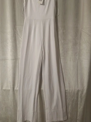 Vit jumpsuit från Bik Bok - Stilren vit jumpsuit från Bik Bok med raka ben och ärmlös design. Jumpsuiten har en enkel och modern look, perfekt för dig som gillar minimalistisk stil. Materialet känns mjukt och följsamt mot kroppen. Finns i storlek 34 och 38