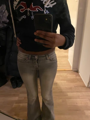 Grå bootcut jeans med slitningar - Säljer ett par grå bootcut jeans med snygga slitningar och ljusa partier framtill. Jeansen har klassisk femficksdesign, låg midja och dragkedja med knapp. Perfekta för en avslappnad och trendig look.
