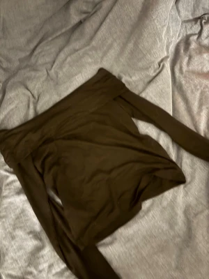 Brun offshoulder topp från 157 - Snygg brun offshoulder topp från 157 i stretchigt material. Toppen har långa ärmar och en tight passform som framhäver axlarna. Perfekt att styla med jeans eller kjol för en trendig look.