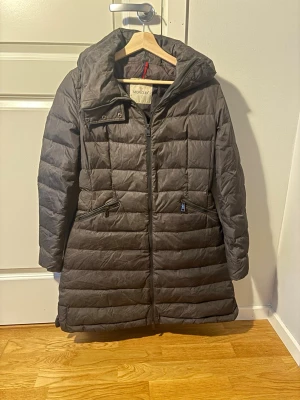 Moncler jacka - Snygg svart dunjacka från Moncler med quiltat mönster, dragkedja framtill och två snedställda fickor med dragkedja. Storlek M. Jackan har en stor huva och är lite längre i modellen, perfekt för kalla dagar. Klassisk och stilren design som håller värmen. Äkta så klart, så om ni är intresserad så hojta till 😄