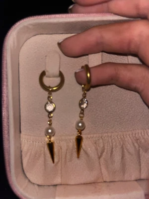 Guldpläterade örhängen med pärlor och spikes - Säljer ett par trendiga örhängen i guldpläterad metall med små vita pärlor, gnistrande stenar och coola konformade spikes. Örhängena har en modern design med ring och hängande detaljer som ger en edgy vibe. Perfekta för dig som vill sticka ut lite extra.