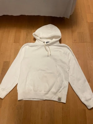 Vit hoodie från Polo Ralph Lauren - Klassisk vit hoodie från Polo Ralph Lauren med huva. Hoodien har en magficka och ribbade muddar vid ärmar och nederkant. Tillverkad i mjukt bomullsmaterial och har en liten patch nertill. Perfekt för en clean och avslappnad stil.