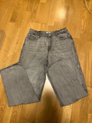 Gråa jeans från Jack & Jones  - Säljer ett par grå jeans från Jack & Jones med rak passform och klassisk femficksdesign. Jeansen har normal midja, knapp- och dragkedjestängning samt detaljerade sömmar på bakfickorna. Tillverkade i denim med en snygg tvättad look.