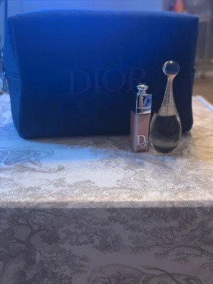 Dior Bundle. Mörkblå neccesär+J’adore 5 ml parfym och Lid addict glow oil 001 pink 2 ml. - Snygg mörkblå necessär från Dior i tygmaterial med diskret logga framtill. Perfekt för att förvara smink, hudvård eller småprylar. Rektangulär form och dragkedja upptill. Stilren och enkel design som känns lyxig. 