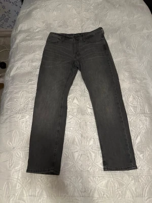 Jack & Jones - Säljer ett par grå jeans med rak passform och fem klassiska fickor. Jeansen har en diskret tvättad look och normal midja. Perfekta för en avslappnad stil och passar till det mesta.