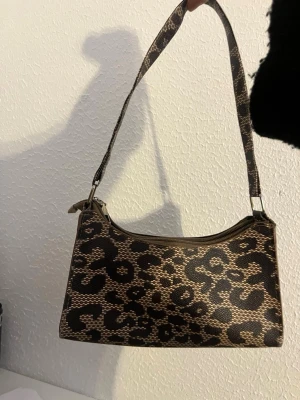 Leopardmönstrad axelväska - Snygg handväska med leopardmönster i brunt och svart. Väskan har en avlång form och ett kort axelband, perfekt för att bära över axeln.