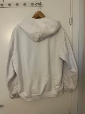 Vit hoodie från Polo Ralph Lauren - Vit hoodie med dragkedja från Polo Ralph Lauren. Klassisk design med huva, fickor framtill och broderad logga på bröstet. Tillverkad i mjukt bomullsmaterial och har ribbade muddar vid ärmslut och nederkant. Perfekt för en avslappnad och stilren look.