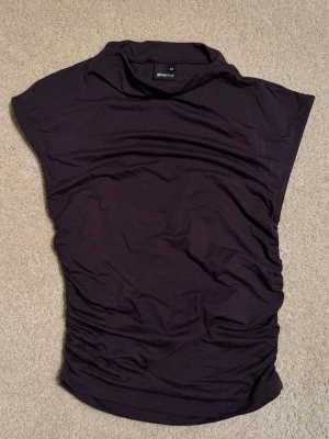 Populär mörkgrå topp från Gina Tricot.  - Populär mörkgrå ärmlös topp från Gina tricot med hög hals och draperade sidor. Tunn och mjuk i materialet. Fin kvalité, använd en gång.