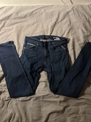 Mörkblå från Replay - Snygga mörkblå skinny jeans från Replay med klassisk femficksdesign och läderpatch bak i midjan. Jeansen har smal passform och stretchigt material. Har storlek L32 och W30. Perfekta för en trendig och avslappnad stil.