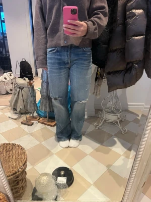 Blå slitna raka jeans - Säljer ett par ljusblå jeans med raka ben och slitningar vid knäna. Jeansen har en klassisk femficksmodell och är tillverkade i denim. Perfekta för en avslappnad och trendig look.