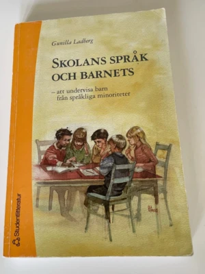 Skolans språk och barnets - Kursbok med titeln 'Skolans språk och barnets' av Gunilla Ladberg. Omslaget är gult och orange med en illustration av barn som sitter runt ett bord. Boken handlar om att undervisa barn från språkliga minoriteter och är tryckt i mjukpärm. Kan finnas översteyckning på insidan av framsida med tusch. 