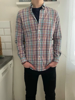 Rutig skjorta från Ralph Lauren - Säljer en klassisk rutig skjorta från Ralph Lauren i bomull. Skjortan har knappar framtill, button-down krage och lång ärm. Färgkombinationen är blå, röd, vit och grön, perfekt för en avslappnad men ändå stilsäker look.