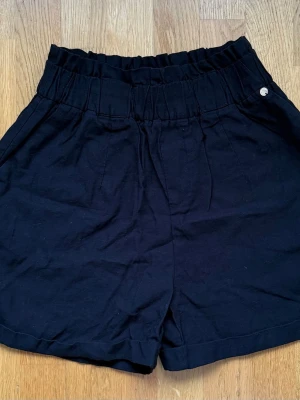 Svarta loose shorts med resårmidja - Säljer ett par svarta shorts med loose passform och bred resår i midjan. Shortsen har fickor på sidorna och en bakficka. Perfekta för sommardagar och enkla att matcha med olika toppar.