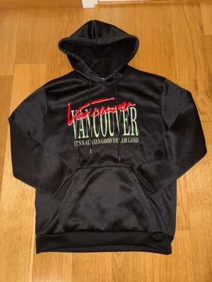 Svart hoodie med Vancouver-tryck - Svart hoodie med huva och känguruficka framtill. Hoodien är i väldigt bra skick och pris kan diskuteras vid snabb affär 