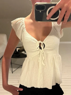 Vit topp/blus - Supersöt vit topp med omlottdesign, knyt framtill och volangdetaljer vid axlarna. Luftigt material och v-ringad skärning. 