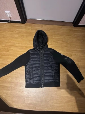 Svart dunväst med huva från Moncler - Hej säljer min Moncler jacka för den har blivit för liten för mig sov de finns ett litet hål de är därför jag säljer den för billigt pris skriv för mer info eller nå 