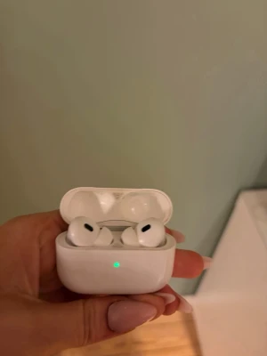 Apple AirPods Pro 2 med laddningsetui - Säljer ett par vita Apple AirPods Pro 2 med trådlöst laddningsetui. Snygg och kompakt design med silikonproppar för bra passform och brusreducering. Perfekta för musik, poddar och samtal. Laddningsetuiet har en LED-indikator på framsidan. Den vänstra airpoden brusar lite, enda defekten. Andra och skalet funkar perfekt
