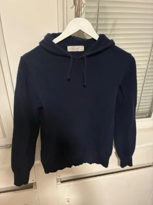 Mörkblå kashmir hoodie Sayless - Mysig mörkblå hoodie från Sayles i mjuk kashmir. Klassisk modell med huva, samt långa ärmar. Perfekt för dig som gillar stilrena och bekväma plagg med en lyxig känsla. Nypris 899 mitt pris 399