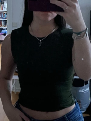 Mörkgrön croppad ärmlös topp - Snygg mörkgrön croppad topp med ärmlös design. Perfekt till jeans eller kjol för en trendig look. Enkel och stilren modell utan synliga detaljer eller mönster.