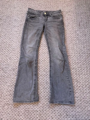 Grå bootcut jeans  - Säljer ett par grå bootcut jeans från Gina Tricot med klassisk femficksmodell och dragkedja. Jeansen har en snygg tvättad look och är tillverkade i denimtyg med bälteshällor. Passar ca 165 cm