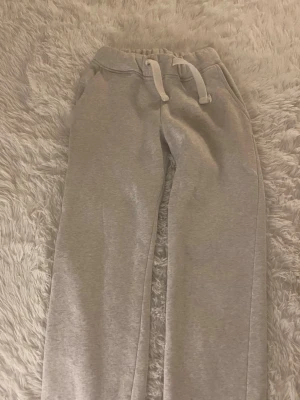 Grå Russemerch mjukisbyxor  - Säljer ett par Russemerch  mjukisbyxor med raka ben och vit dragsko i midjan. Byxorna har fickor på sidorna och är gjorda i mjukt sweatshirtmaterial, perfekta för chill dagar hemma eller när du vill vara extra bekväm.
