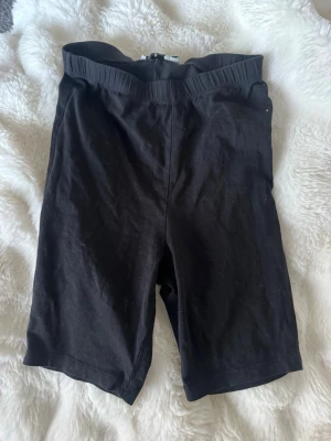 Svarta cykelshorts med resårmidja - Svarta cykelshorts med elastisk midja och enkel, stilren design. Perfekta för en avslappnad look eller till träning. Tillverkade i mjukt material som ger skön passform och rörelsefrihet.  Storlek xxs från nelly. 