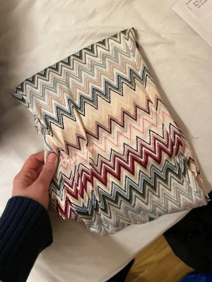 Mönstrade rosa leggings med zigzag-mönster  - Säljer ett par leggings med färgglatt zigzag-mönster i nyanser av vinrött, olivgrönt, grått, blått och vitt. De har hög midja och är tillverkade i ett stretchigt, mjukt material som sitter skönt på kroppen. Perfekta för dig som gillar statement-plagg och vill sticka ut.